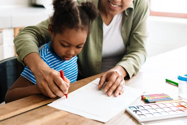 Mutlu bir anne, kızıyla birlikte ev mutfağında resim çizer.