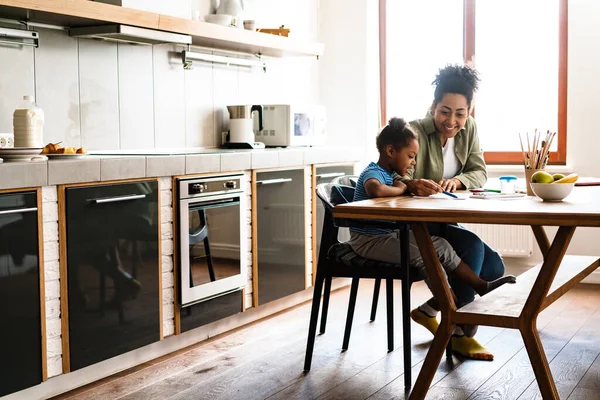 Mutlu bir anne, kızıyla birlikte ev mutfağında resim çizer.