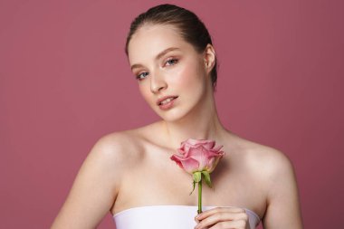 Pembe arka planda saklanmış bir gülle poz veren çekici genç bir kadının güzel portresi.