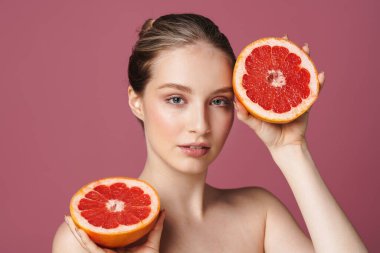 Pembe arka planda greyfurtla poz veren çekici genç bir kadının güzel portresi.