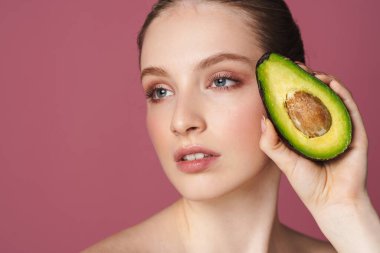 Doğal yollarla cildine özen gösteriyorum. Pembe izole edilmiş arka planda avokadoyla poz veren güzel bir kadının stüdyo portresi.