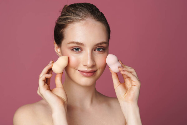 Закрыть портрет красотки привлекательной молодой женщины, позирующей с косметическими губками, изолированными на розовом фоне