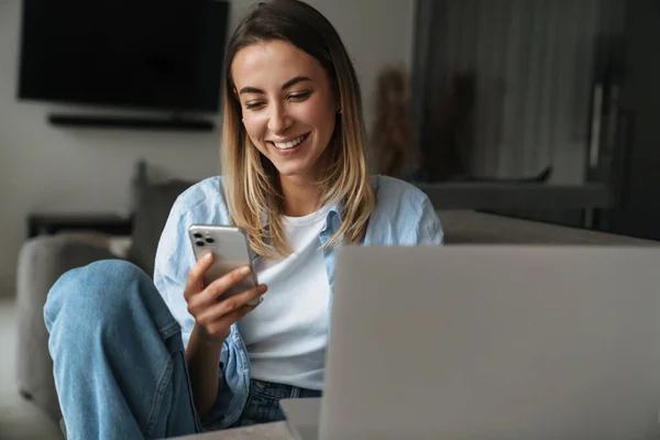 Glückliche Junge Frau Benutzt Handy Während Sie Hause Mit Laptop — Stockfoto