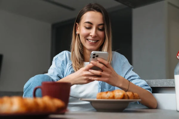 Vidám Fiatal Lány Mobiltelefont Használ Miközben Otthon Reggelizik Konyhában — Stock Fotó