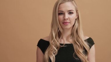 Ciddi bir sarışın kadın, stüdyodaki bej bir duvarın üzerinde tek başına kameraya bakarken olumsuz cevap veriyor.