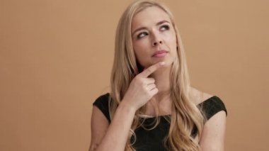 Düşünen sarışın bir kadın, stüdyodaki bej bir duvarın arkasında izole edilmiş bir fikirle çıkageliyor.