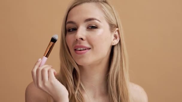 Leende Blond Kvinna Applicerar Kosmetika Ansiktet Stående Isolerad Över Beige — Stockvideo