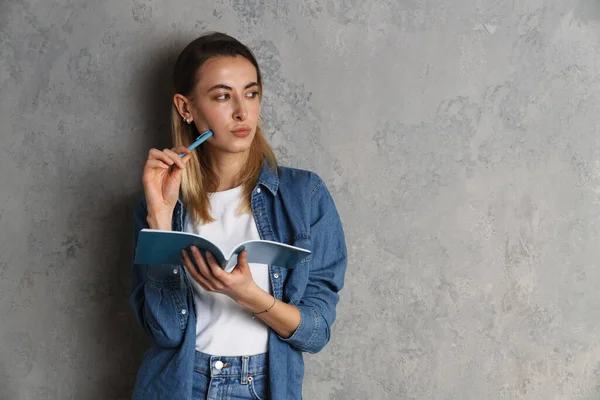 Pensive Attractive Young Casual Woman Taking Notes While Standing Isolated — Stock Photo, Image