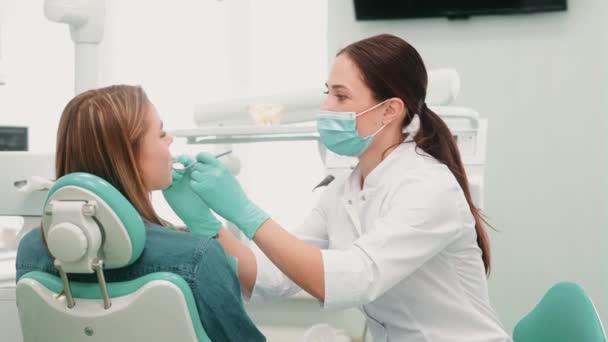 保護マスクを着た歯医者がクリニックで患者の歯を治療しています — ストック動画