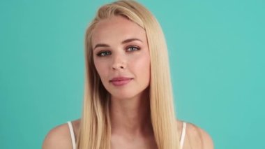 Pozitif sarışın bir kadın derisine bakıyor. Stüdyonun mavi duvarında tek başına duruyor.