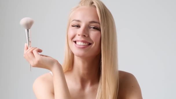 Positiv Ung Blond Kvinna Applicerar Makeup Med Puderborste Stående Isolerad — Stockvideo