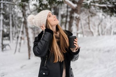 Mutlu güzel kız, kış ormanlarında yürürken kahve içer.