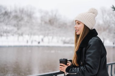 Mutlu güzel kız kış parkında yürürken kahve ısmarlıyor.