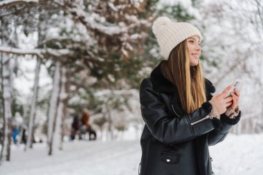 Mutlu güzel kız, kış ormanlarında yürürken cep telefonu kullanıyor ve gülümsüyor.