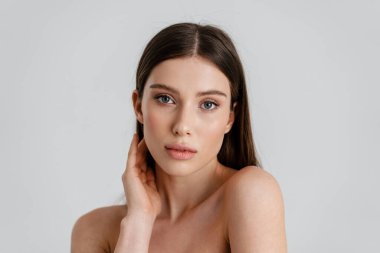 Güzel üstsüz kız beyaz arka planda yalnız poz veriyor ve kameraya bakıyor.