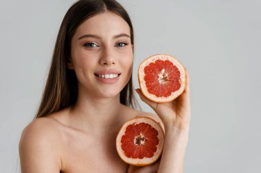 Beyaz arka planda izole edilmiş greyfurtla poz verirken gülümseyen mutlu üstsüz kız.