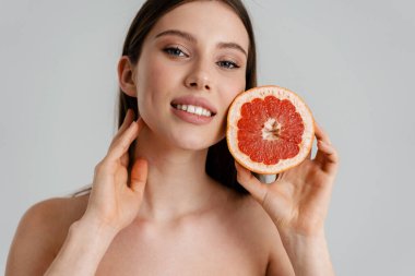 Beyaz arka planda izole edilmiş greyfurtla poz verirken gülümseyen mutlu üstsüz kız.