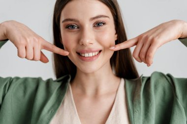 Mutlu beyaz kız gülümsüyor ve beyaz arka planda izole edilmiş yanaklarını işaret ediyor.