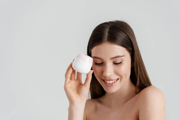 Happy shirtless nice girl smiling while posing with facial cream isolated over white background