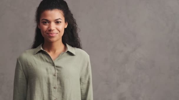 非洲裔美国妇女笑着站在工作室灰色的墙壁上 手里拿着什么东西 — 图库视频影像