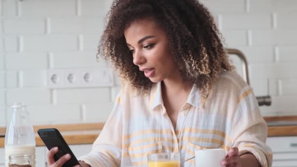 Una Hermosa Mujer Afroamericana Está Usando Teléfono Inteligente Mientras Desayuna — Vídeo de stock