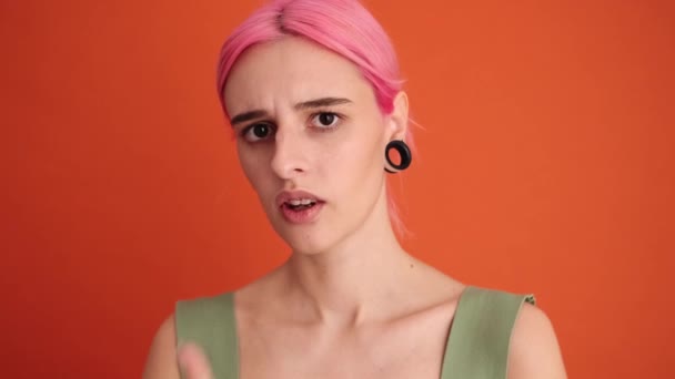 一位有着一头粉色头发的严肃的年轻女子站在摄影棚的橙色墙上做着沉默的手势 — 图库视频影像