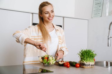 Mutfakta taze salata hazırlarken gülümseyen neşeli sarışın kadın.