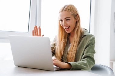 Bilgisayarlı, gülümseyen genç bir kadın ev telefonuna el sallayarak el sallıyor.