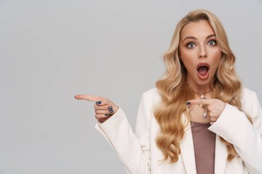 Gri arka planda izole edilmiş, ceketli, güzel, şok olmuş bir kız.