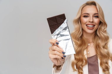 Gri arka planda saklı çikolatayla poz verirken gülümseyen mutlu muhteşem kadın.