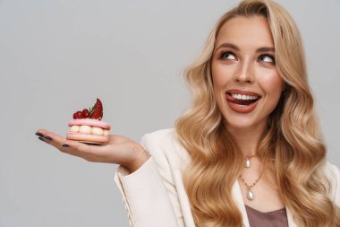 Gri arka planda saklanmış pastayla poz verirken gülümseyen mutlu muhteşem kadın.