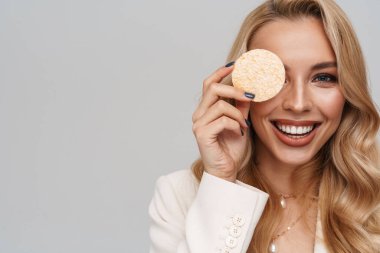 Gri arka planda kozmetik süngerle poz verirken gülümseyen mutlu muhteşem kadın.