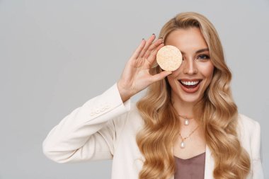 Gri arka planda kozmetik süngerle poz verirken gülümseyen mutlu muhteşem kadın.