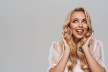 Güzel, gülümseyen sarı saçlı, elbiseli genç bir kadın mavi arka planda tek başına poz veriyor.