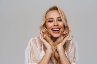 Güzel, gülümseyen sarı saçlı, elbiseli genç bir kadın mavi arka planda tek başına poz veriyor.