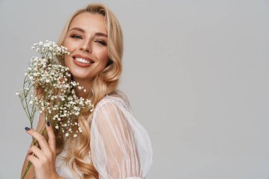 Gri arka planda saklı çiçeklerle poz verirken gülümseyen güzel mutlu kız.