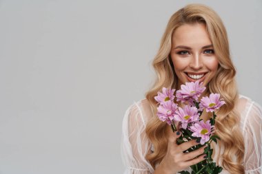 Gri arka planda saklı çiçeklerle poz verirken gülümseyen güzel mutlu kız.