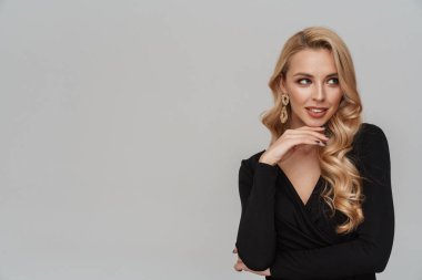 Lüks küpeli mutlu bir kız. Gri arka planda yalnız başına poz veriyor ve bakıyor.