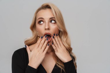 Gri arka planda izole edilmiş kameraya şaşkınlığını ifade ederken ağzını kapatan şaşkın kız.