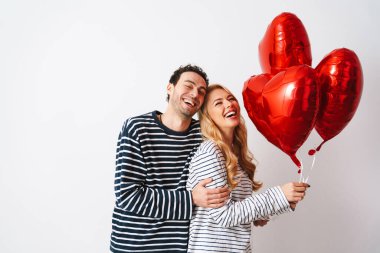 Mutlu romantik çift gülüyor, beyaz arka planda izole edilmiş kalp balonlarıyla poz veriyor.
