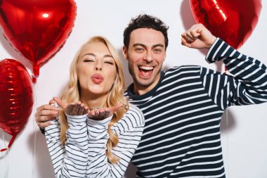 Mutlu çift, beyaz arka planda izole edilmiş kalp balonları ile poz verirken eğleniyor.