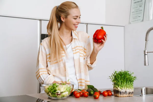 Mulher Loira Alegre Mostrando Pimentão Enquanto Prepara Salada Fresca Cozinha — Fotografia de Stock