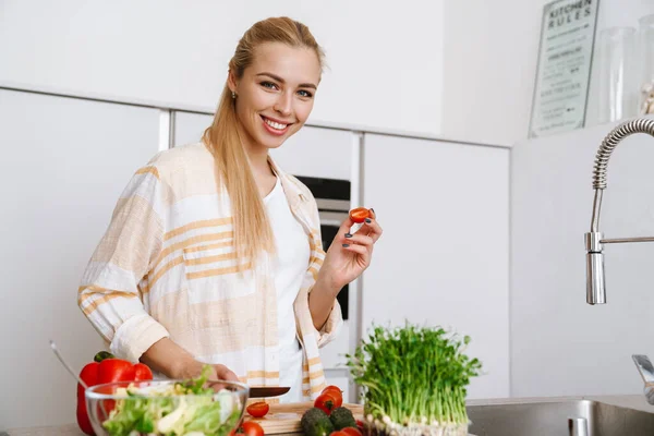 Mulher Loira Alegre Segurando Tomate Enquanto Prepara Salada Fresca Cozinha — Fotografia de Stock