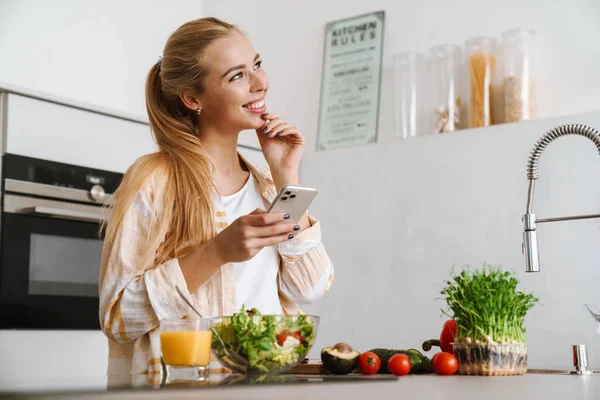 一个快乐迷人的女人在厨房里用手机做健康沙拉的肖像 — 图库照片