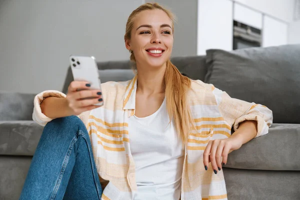 Mujer Rubia Feliz Sonriendo Usando Teléfono Celular Mientras Sienta Piso — Foto de Stock