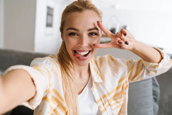 Šťastná Blondýna Žena Ukazující Mír Zpěv Při Focení Selfie Doma — Stock fotografie