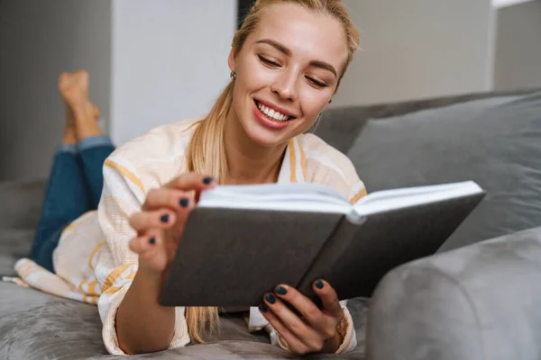 Mujer Feliz Sonriendo Leyendo Libro Mientras Está Acostado Sofá Casa — Foto de Stock