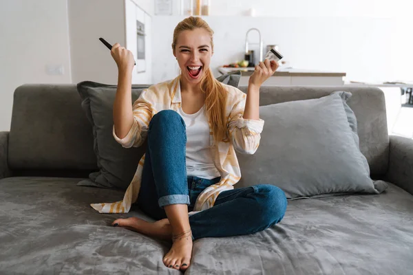 Excited Woman Holding Credit Card While Watching Remote Control Home — Stock Photo, Image