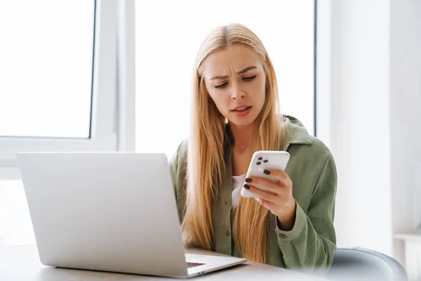 Zmatený Frustrovaný Mladý Žena Pomocí Mobilního Telefonu Zatímco Sedí Stolu — Stock fotografie