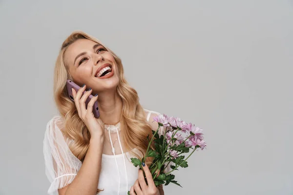 Śmiejąca Się Blondynka Rozmawia Przez Komórkę Trzymając Kwiaty Szarym Tle — Zdjęcie stockowe